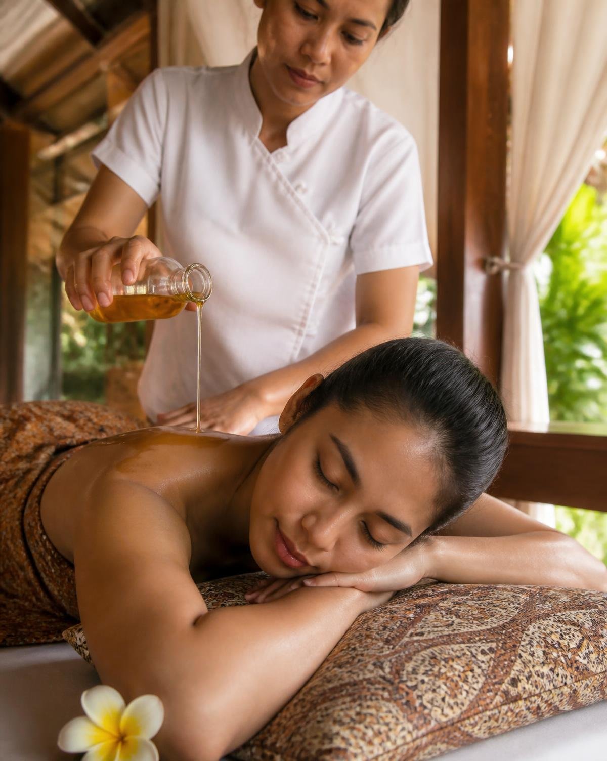 Warm oil poured during a four hand nuru massage by two therapists in a private Goa spa suite